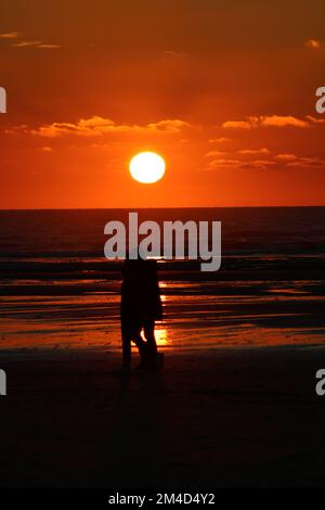 Une photo verticale d'un magnifique coucher de soleil avec un couple marchant sur la plage de Hardelot, France Banque D'Images