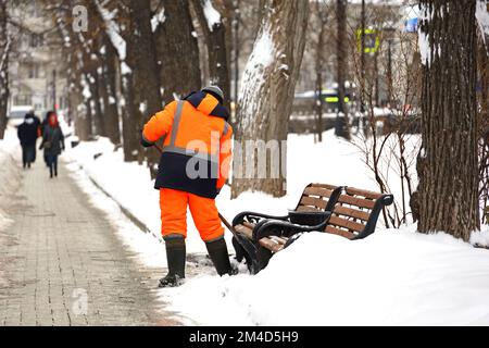 Un employé nettoie la neige dans les rues de la ville après une chute de neige. Homme avec une pelle dans le parc d'hiver Banque D'Images