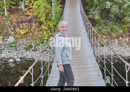 Femme de randonneur senior souriante sur pont suspendu sur fond de nature. Banque D'Images