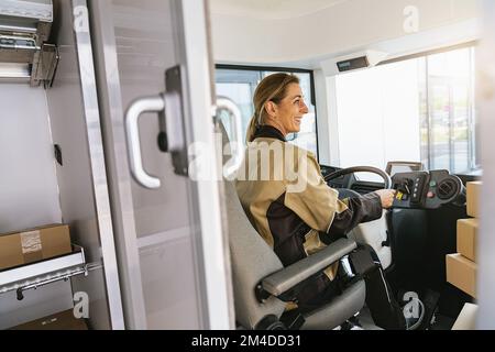 Femme de livraison conduisant une fourgonnette avec des groupes sur le siège avant. Bonne femme de coursier dans le camion. Portrait d'un messager express confiant qui conduit sa livraison Banque D'Images