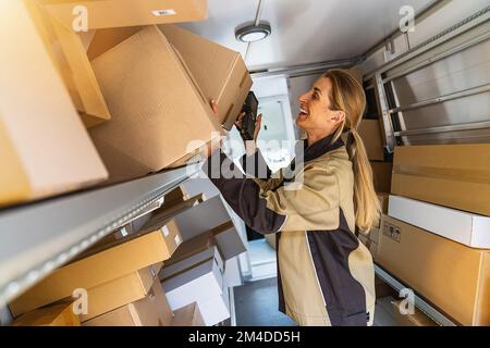 femme agent de livraison cherchant dans ses colis de camionnette pour les livrer à un client Banque D'Images