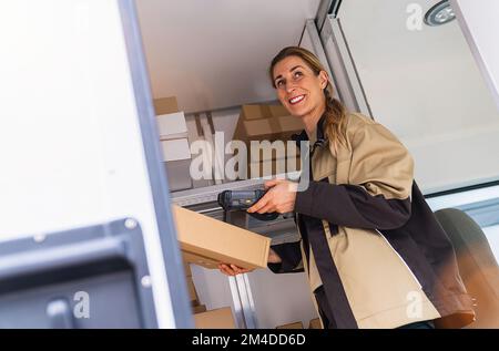 une femme de livraison scanne le code-barres avec un lecteur de code-barres à l'intérieur de sa camionnette sur un colis Banque D'Images