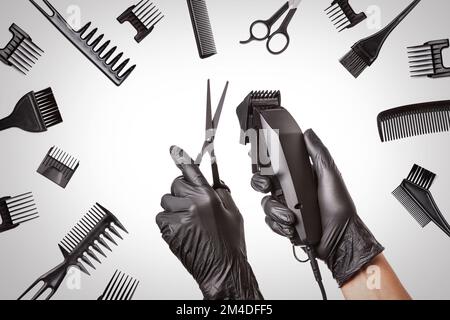 Coiffeurs mains en gants de caoutchouc noir tient la tondeuse cheveux et les ciseaux entourés d'accessoires de coiffure professionnels, gros plan Banque D'Images