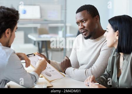 Portrait d'un homme noir tenant une planchette à pince tout en discutant du projet lors d'une réunion d'affaires avec l'équipe Banque D'Images