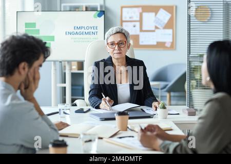 Portrait d'une femme d'affaires senior assise à la tête de la table lors d'une réunion d'affaires avec l'équipe Banque D'Images