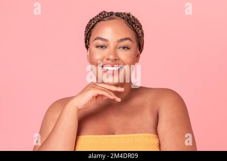 Concept de beauté naturelle. Portrait d'une femme noire et de taille plus heureuse posant sur fond rose studio et souriant à l'appareil photo Banque D'Images