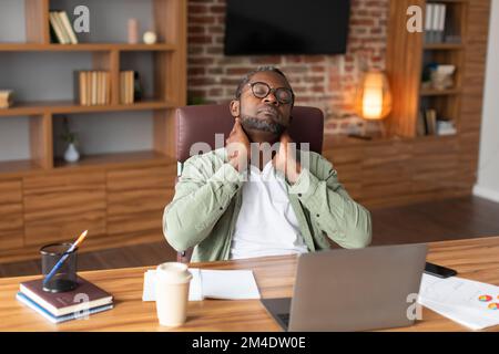 Homme d'affaires noir adulte fatigué dans des lunettes souffrant de douleurs au cou, inconfort de longues heures de sédentarité Banque D'Images