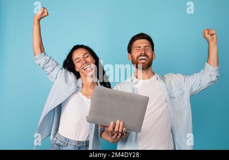 Un jeune couple européen plein d'émotions satisfait avec un ordinateur portable fait un geste de réussite et de victoire, profitez de gagner ensemble Banque D'Images