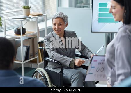 Portrait d'une femme d'affaires en fauteuil roulant souriante lors d'une réunion d'équipe Banque D'Images