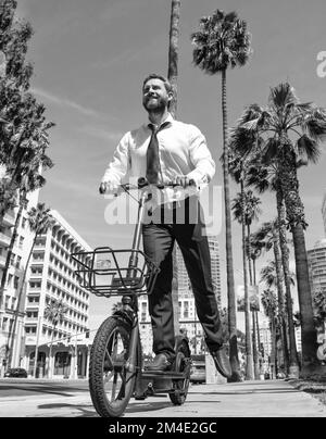 Un gars heureux en tenue de formalwear scooter électrique sur le trottoir, le démarrage Banque D'Images