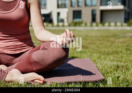 Gros plan d'une jeune femme assise dans une position lotus éclairée par la lumière du soleil tout en appréciant le yoga à l'extérieur sur l'herbe verte, l'espace de copie Banque D'Images