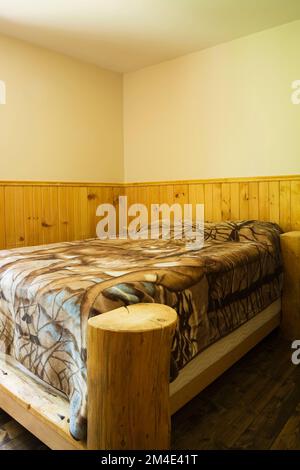 Lit à baldaquin rustique dans une petite chambre à l'étage avec des planchers teintés bruns nuancés à l'intérieur de la maison en rondins. Banque D'Images