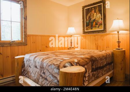 Lit à baldaquin rustique dans une petite chambre à l'étage avec des planchers teintés bruns nuancés à l'intérieur de la maison en rondins. Banque D'Images