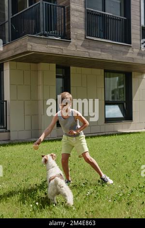 Portrait complet d'un garçon souriant jouant avec un chien mignon sur la pelouse au soleil Banque D'Images