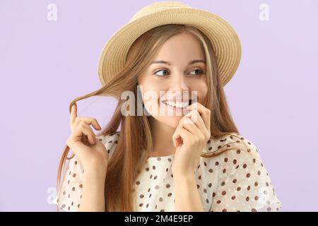 Jeune femme en chapeau mordant des ongles sur fond lilas, gros plan Banque D'Images