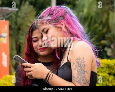 Medellin, Antioquia, Colombie - 14 novembre 2022: Les jeunes femmes colombiennes avec des cheveux rouges et roses regardent un téléphone cellulaire Banque D'Images