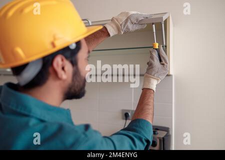 La vue arrière de l'ouvrier en uniforme est d'assembler le mobilier sur la cuisine. Concept de réparation Banque D'Images