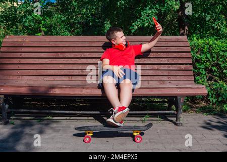 Garçon assis sur le banc et communique par chat vidéo à l'aide d'un smartphone et d'Internet. Banque D'Images