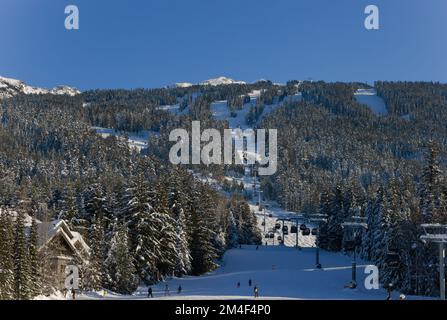 Vue panoramique sur les montagnes enneigées - les surfeurs et les skieurs se trouvent sur les pistes et les remontées mécaniques. Station de ski à Whistler, Canada Banque D'Images