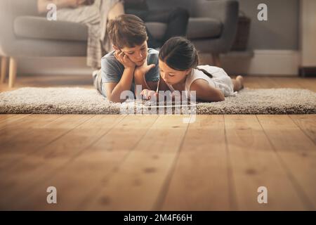 Grandir avec des jouets numériques. un adorable frère et une sœur utilisant une tablette numérique à la maison avec leurs parents en arrière-plan. Banque D'Images