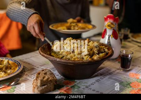 Personne servant un plat portugais typique avec du poisson à la morue, de l'huile d'olive et des pommes de terre servi dans un pot en terre battue sur une table rustique traditionnelle Banque D'Images