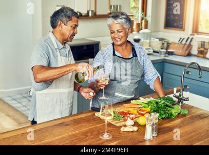 Qui a dit que la préparation du dîner doit être une corvée. un couple heureux et mature qui boit du vin tout en cuisinant un repas à la maison. Banque D'Images
