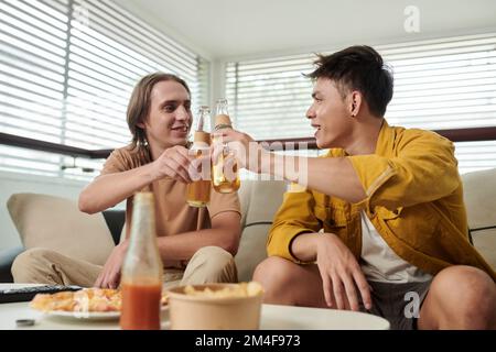 Les jeunes hommes se trinquer avec des bouteilles lorsqu'ils boivent de la bière à la maison Banque D'Images