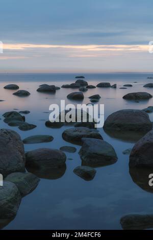 Heure bleue après le coucher du soleil sur la mer Baltique rocheuse coût. Petites pierres et gros rochers dans la mer. Photo à exposition longue. Banque D'Images