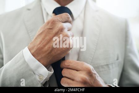 Les touches de finition. un homme d'affaires méconnaissable portant un costume tout en ajustant sa cravate avant de partir au travail à la maison pendant la journée. Banque D'Images