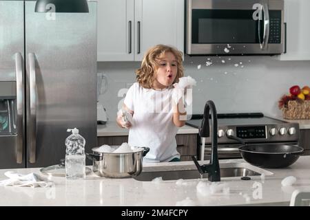 Les enfants lave les plats près de l'évier dans la cuisine. L'enfant avec une éponge avec du liquide vaisselle fait la vaisselle à la cuisine à la maison en utilisant une éponge de lavage et Banque D'Images