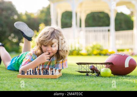 Jeux d'été et activités de plein air pour les enfants. Enfant jouant au jeu d'échecs dans l'arrière-cour du printemps, en posant sur l'herbe. Jeu d'échecs concentré. Jeu d'enfant Banque D'Images