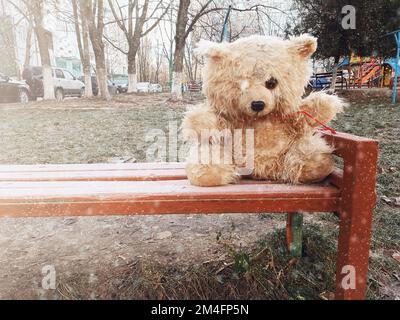 Jouet mou endommagé. Ours en peluche abandonné dans la rue. Poupée seule en hiver s'assoit sur un banc. Banque D'Images