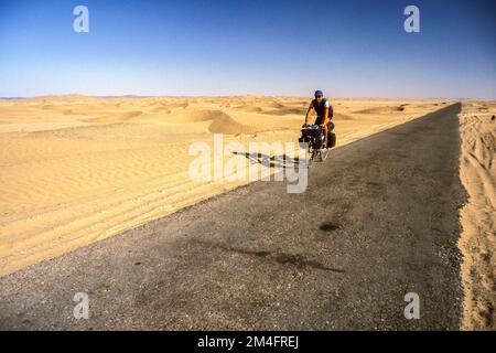 Cycliste solitaire entre dunes de sable errantes sur la route entre Taftan et Quetta. Banque D'Images