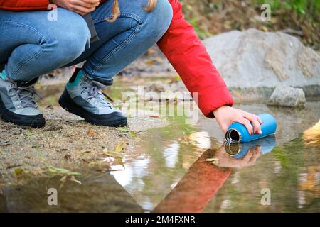 Un trekker méconnaissable remplit une bouteille d'eau brute dans une rivière. Banque D'Images