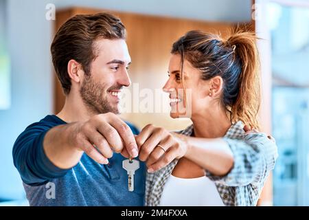 Notre nouvelle vie commence maintenant. un jeune couple joyeux tenant une clé ensemble à leur nouvelle maison tout en se tenant à l'intérieur pendant la journée. Banque D'Images