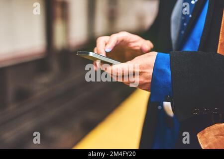 Il semble que la messagerie instantanée soit toujours bonne avec le temps. un homme méconnaissable envoie un message texte sur son téléphone en attendant qu'un train entre au travail le matin. Banque D'Images