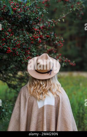 Femme avec chapeau et poncho debout sous l'arbre d'aubépine dans la nature d'automne. Mode hippie Banque D'Images