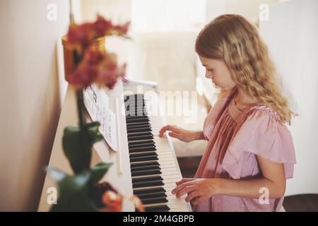 Portrait mignon courbé blond adolescente fille jouant des clés piano à la maison intérieur lumineux Banque D'Images