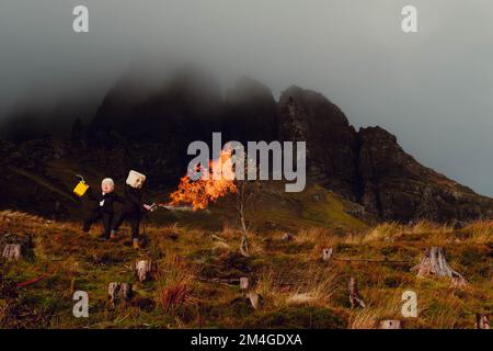 Île de Skye, Écosse, Royaume-Uni. 24th octobre 2021. Une personne avec un masque Boris Johnson et une autre avec un réservoir d'huile pour une tête, représentant les compagnies pétrolières, utilisent un lanceur de flamme pour brûler un arbre qui représente le dernier arbre sur terre. Cette manifestation théâtrale a été organisée par Ocean Rebellion, un mouvement frère de la rébellion d'extinction, dans le vieil homme de Storr, île de Skye en Écosse, avant le début de la CdP 26 à Glasgow. Banque D'Images