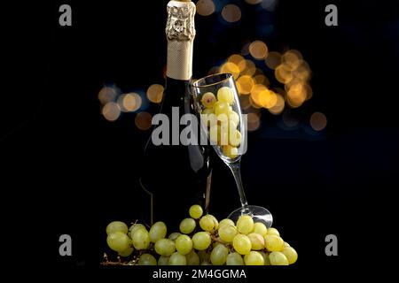 Cava ou bouteille de champagne avec verre et raisins sur fond noir avec lumières bokeh, pour la Saint-Sylvestre Banque D'Images