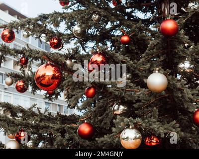 Gros plan d'un sapin de noël à la décoration festive avec des boules rouges et beiges sur fond flou. Banque D'Images