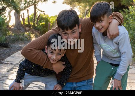 Joyeux adolescent dans des vêtements décontractés souriant et embrassant jeune frère tout en s'amusant sur le chemin pavé en soirée dans le parc Banque D'Images