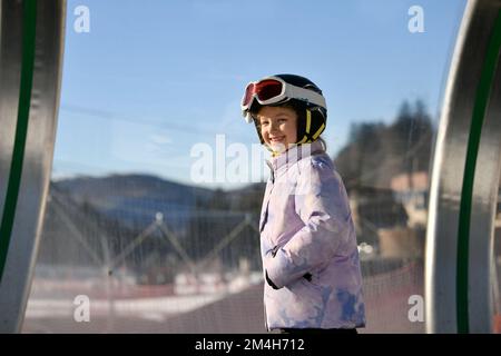 Une jeune fille à skis se tient sur un remonte-pentes de tapis dans une tunique Banque D'Images