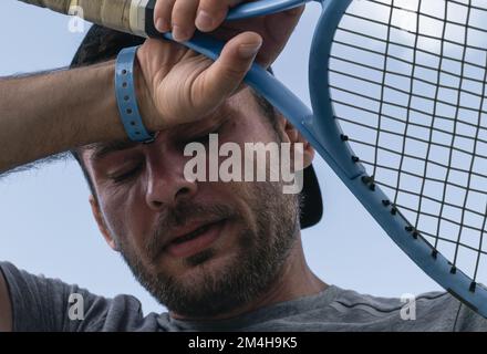 Portrait de la tête du joueur de tennis, l'athlète masculin tient la raquette de tennis dans sa main et élimine la sueur du front. Sportif fatigué, sportif et sain Banque D'Images