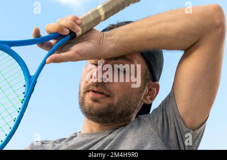 Homme barbu adulte joueur de tennis élimine la transpiration du front, photographie rapprochée de l'athlète fatigué après le match de tennis. Banque D'Images