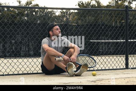 Homme joueur de tennis assis sur le court de tennis et attendant son tour pour jouer au tennis. Banque D'Images