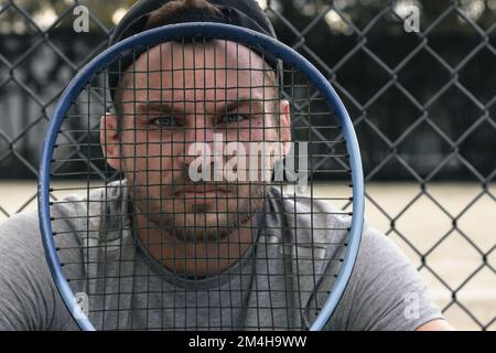 Homme regardant à travers la raquette de tennis, sérieux visage masculin. Banque D'Images