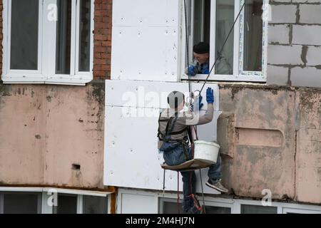 Tiraspol, Moldavie - 10 décembre 2022 : un constructeur de haute altitude isole la façade d'un immeuble d'appartements en plastique mousse. Maison isolante aérée Banque D'Images