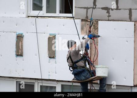 Tiraspol, Moldavie - 10 décembre 2022 : un constructeur de haute altitude isole la façade d'un immeuble d'appartements en plastique mousse. Maison isolante aérée Banque D'Images