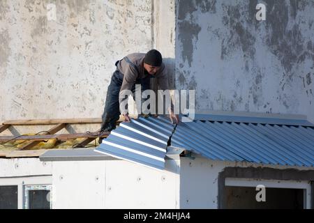 Tiraspol, Moldova - 13 décembre 2022 : le constructeur couvre le toit avec une tôle d'aluminium ondulée. Les travailleurs construisent sur le toit du châssis pour le balcon en décembre. Banque D'Images